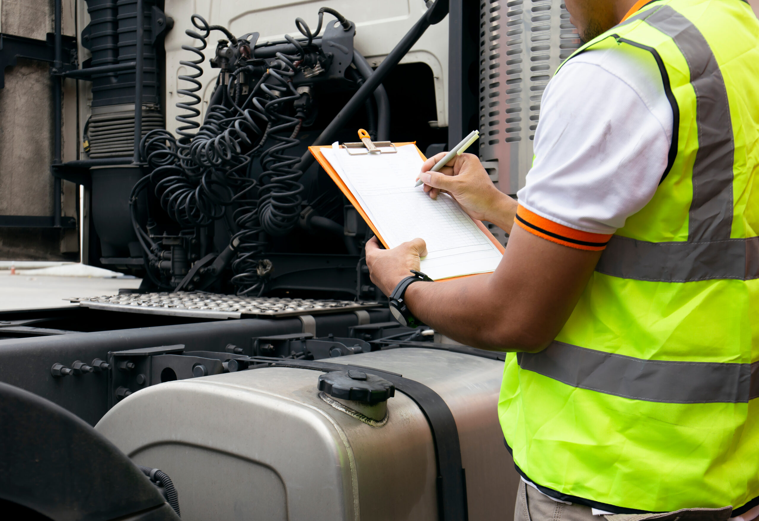 Image of a man wearring ang safety vest while taking down notes for truck maintenance